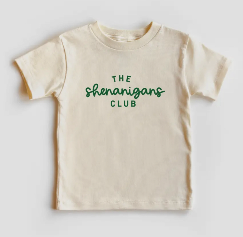 A cream colored short sleeve shirt that says The Shenanigans Club in green font.